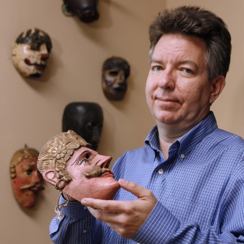 Stephen Houston holding a mask in front of a wall of masks