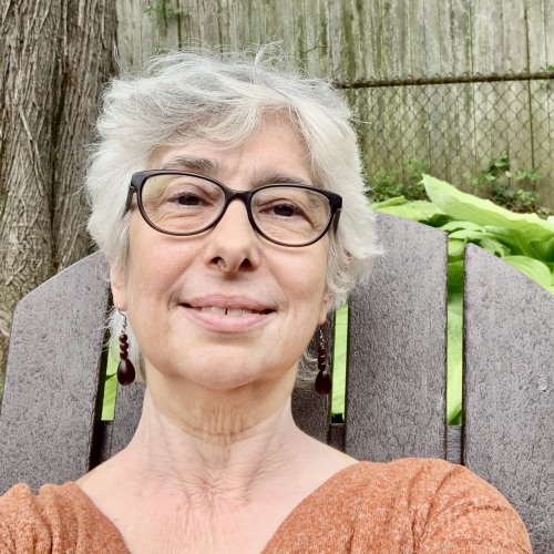 Woman on a wooden chair with short gray hair and glasses, smiling