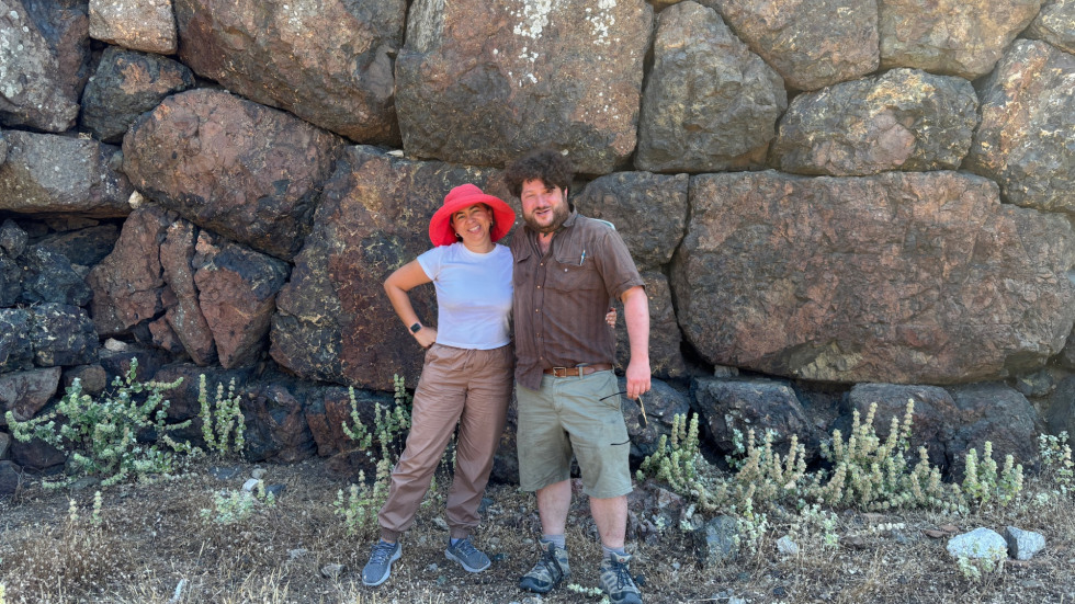 2 figures in front of ancient stone wall