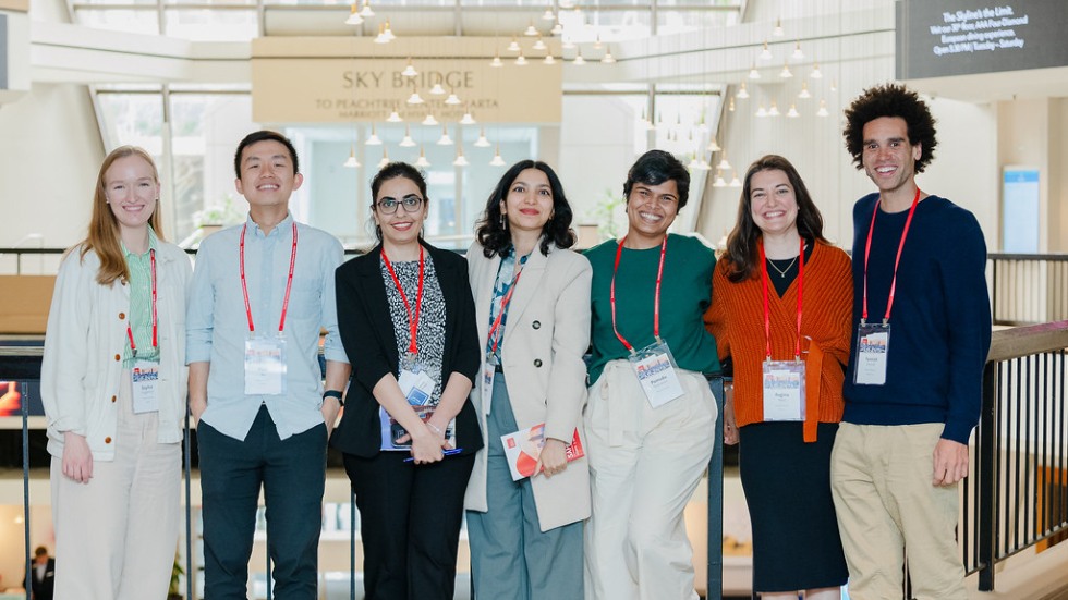 Seven people standing in a brightly lit atrium smiling